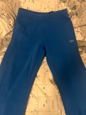 Blå mjukisbyxor från Lacoste scheme - Snygga blå mjukisbyxor från Lacoste med regular fit och klassisk krokodil-logga på benet. Tillverkade i mjukt och skönt material med borstad insida för extra komfort. Perfekta för chill dagar eller när du vill ha en clean och avslapp…ad look.