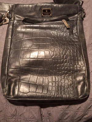 Svart axelväska i crocopräglat läder - Snygg svart axelväska från Tiger of Sweden i crocopräglat läder. Väskan har justerbar axelrem, dragkedja framtill och en metallbricka med logga. Lite sliten nertill. Priset kan diskuteras 🫶😊