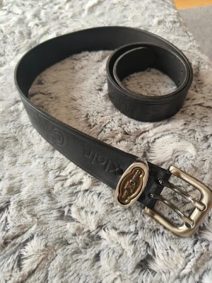  svart skärp från Calvin Klein - Snyggt svart bälte från Calvin Klein med präglad logga längs remmen. Spännet är i metall med en unik detalj och Calvin Klein-märkning. Perfekt accessoar för att lyfta din outfit.