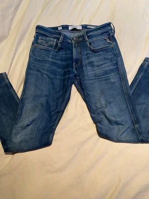 Blå raka Replay jeans - Säljer ett par klassiska blå jeans från Replay med rak passform och fem fickor. Jeansen har snygga slitningar och är gjorda i denim medul en autentisk tvätt. Perfekta för en avslappnad och stilren look.