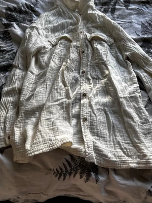 Vit skjorta i bomull från Zara - Luftig vit skjorta från Zara i storlek 152, tillverkad i mjuk bomull. Skjortan har långa ärmar, knappar framtill och två bröstfickor. Perfekt för en avslappnad och stilren look.