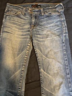 Blå slitna jeans med tvättade detaljer - Säljer ett par blå jeans med snygga slitningar och tvättade detaljer. Jeansen har klassisk femficksmodell, låg midja och utsvängda ben. Perfekta för en avslappnad och trendig look.