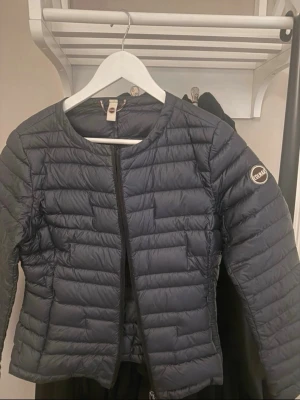 Mörkblå dunväst från Colmar - Snygg mörkblå dunväst från Colmar med quiltad design och rund halsringning. Västen har diskret logga på ärmen och dragkedja framtill. Tillverkad i lätt och glansigt material som ger en modern look. Perfekt för lager-på-lager-stil.