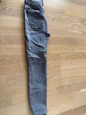 Gråa raka jeans - Säljer ett par gråa jeans med rak passform och klassiska bakfickor. Jeansen har en enkel design utan synliga slitningar eller dekorationer. Perfekta för en clean och stilren look.