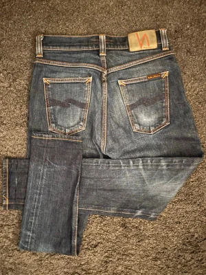Nudie Jeans Brute Knut – Unik inbodd tvätt & grymma fades! (W27) - Grymma Nudie Jeans! Unik, inbodd tvätt med snygga kontraster och en riktig premiumkänsla! 🧵 Märke & Modell: Nudie - Brute Knut 📏 Storlek & Passform: W27 L28. Avslappnad slim.  🧩 Material: 99% bomull / 1% elastan 📐 Mått: Midja: 35 cm Innerbens-sömm: 65 cm Ytterbenslängd: 91 cm ✅ Skick: 8/10 – Mycket fint skick med schyssta fades. ✨ Detaljer: Tydliga orangea sömmar och en skinnpatch. 💰 Nypris: Ca 1600kr 🧍‍♂️ Referens: Passar 167-172 cm. ‼️ Skickas samma dag eller senast dagen efter betalning‼️