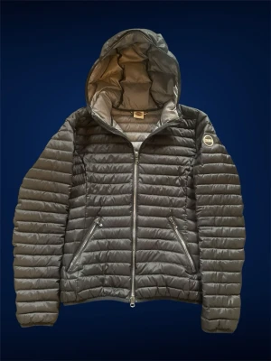 Svart dunjacka med huva från Colmar - Snygg svart dunjacka från Colmar med quiltad design och fast huva. Jackan har två dragkedjeförsedda fickor framtill och en logotyp på ärmen. Lätt och smidig modell som passar perfekt till vår & höstdagar.