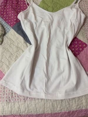 Vit linnetopp med smala axelband - Enkel och stilren vit linnetopp med smala axelband och rak passform. Perfekt att matcha med jeans eller kjol för en clean look. Tillverkad i mjuk bomull som känns skön mot huden.