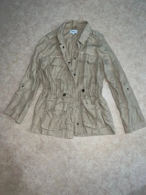 Beige lätt jacka från ONLY xs/s - Snygg och lätt jacka i beige färg från ONLY. Modellen har flera fickor framtill och dragsko i midjan som ger en fin passform. Perfekt som vår- och höstjacka.