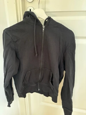 Svart zip hoodie med huva - En svart hoodie med dragkedja framtill och huva med snören. Köpt på bikbok