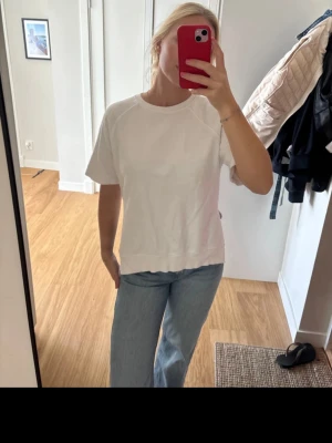 Kortärmad tjocktröja  - Vit t-shirt i collegematerial med korta ärmar och rund hals. Modellen har en slits på sidan som ger en cool detalj och en lite loose passform. Perfekt för dig som gillar enkel och stilren design.