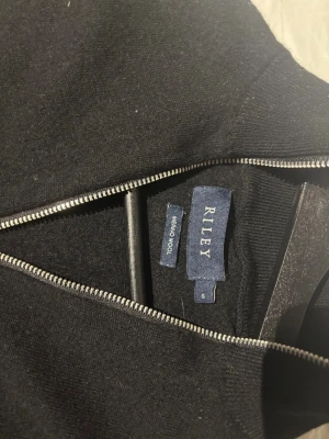 Svart merinoullströja med dragkedja Riley - Svart tröja från Riley i 100% merinoull med hel dragkedja framtill. Riktigt snygg och stilren tröja. Står storlek S men sitter som xs, bara använd en gång inga och fri från defekter.