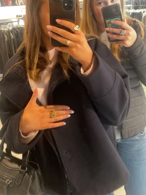 Mörkblå kappa med bred krage - Snygg mörkblå kappa med bred krage och avslappnad passform. Kappan har en stilren design som passar perfekt till jeans eller klänning. Perfekt för dig som vill ha en trendig vår jacka i garderoben.