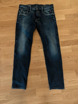 Replay mörkblå raka jeans med slitningar - Säljer ett par mörkblå replay jeans med raka ben och snygga slitningar framtill. Jeansen har klassiska fem fickor, kontrastsömmar och knappgylf. Materialet är denim i bomull. Perfekta för en avslappnad och trendig look. Fick dem i julklapp men kommer aldrig till användning använda 1 gång. 