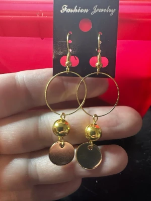 Guldiga cirkelörhängen med pärldetalj - Säljer ett par trendiga örhängen i guldfärgad metall med stora cirklar, blanka guldfärgade pärlor och runda plattor som hänger ned. Perfekta för dig som gillar statement-smycken och vill addera lite extra bling till din look.