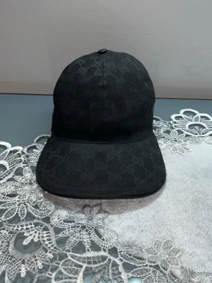 Svart Gucci keps med GG-mönster - Snygg svart keps från Gucci med diskret GG-monogram över hela kepsen.  den är k strl S och jätte bra skick och den är äkta och chippen kommer med pris kan alltid diskuteras 