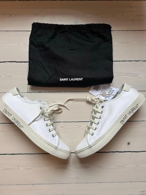 Vita Saint Laurent canvas sneakers - Snygga vita sneakers från Saint Laurent i canvas med klassisk låg profil och vita snören. Märkets logga syns på sidan och innersulan. Skorna har en stilren design och kommer med svart dustbag.