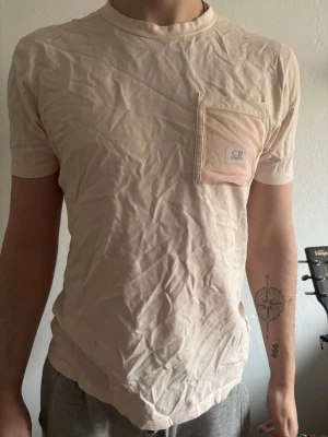 Rosa t-shirt med meshficka - Säljer en ljus rosa t-shirt från CR med en unik meshficka på bröstet. T-shirten har rund halsring spännande detalj med nätficka och är tillverkad i mjukt bomullsmaterial.