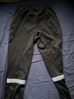 Svarta träningsbyxor Nike Dri-FIT - Säljer ett par svarta träningsbyxor från Nike med Dri-FIT-material som transporterar bort fukt. Byxorna har elastisk midja och vita rutiga detaljer vid bensluten. Perfekta för löpning eller gympass. CR7
