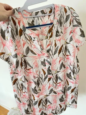 Blommig kortärmad blus Soyaconcept - Säljer en luftig blus från Soyaconcept med korta ärmar. Blusen är vit med rosa, bruna och gråa blommönster samt små svarta prickar. V-ringad hals och lätt material som känns skönt mot huden. Perfekt för en fräsch och somrig look.