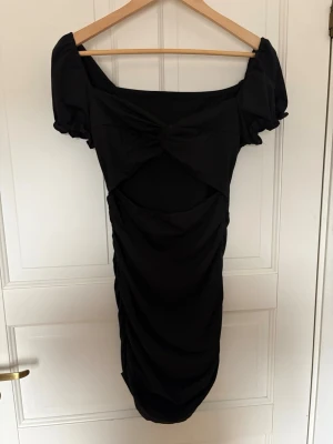 Svart kort klänning med puffärm - Trendig svart kort klänning med puffärmar och twistad detalj framtill. Klänningen har en snygg drapering längs kjolen