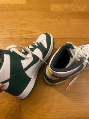 Nike Dunk High vit och grön  - Ett par Nike dunk high sneakers i storlek 39. Skorna är använda och har några missfärgningar och är lite creasade längst fram, se sista bilderna. Nypris 1600kr. Förhandlar gärna om priser. Har katter hemma!!!