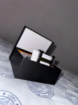 Vitt bälte med silverfärgat H-spänne - Säljer ett stilrent vitt bälte med ett stort, silverfärgat H-format spänne. Bältet kommer i en snygg svart presentask med guldfärgad insida. Perfekt accessoar för att lyfta din outfit.