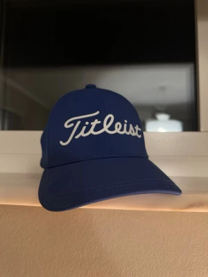 Blå Titleist keps använd någon gång bara - Snygg blå keps från Titleist med klassisk böjd skärm och vit broder soppskrift framtill. Kepsen har ventilerande hål och justerbar baksida för perfekt passform. Perfekt för golfbanan eller som cool accessoar till vardagslooken.