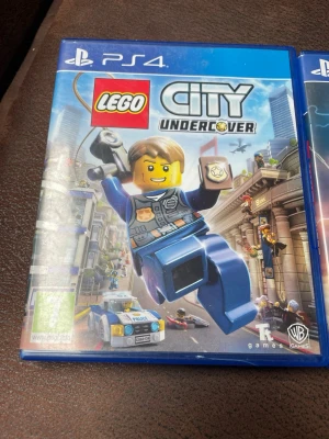 LEGO City Undercover till PS4 - Säljer spelet LEGO City Undercover till PlayStation 4. Ett actionäventyr där du spelar som polis i en öppen värld fylld med LEGO-bilar, byggnader och karaktärer. Omslaget är blått med färgglada LEGO-figurer och typisk LEGO-design. Perfekt för dig som gillar humor och äventyr.