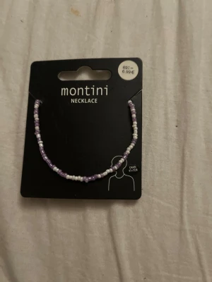 Lila och vitt pärlhalsband Montini - Sött halsband från Montini med små pärlor i lila och vitt. Halsbandet har en enkel och trendig design som passar perfekt till olika stilar. Kedjan är tunn och smidig, och pärlorna ger en lekfull touch till din outfit.