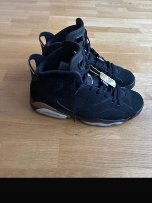 Svarta Air Jordan 6 sneakers - Snygga svarta Air Jordan 6 sneakers med gulddetaljer och klassisk hög siluett. Skorna har ovandel i mocka och detaljer i guld på snörningen samt en vit och svart sula. Perfekta för dig som gillar streetwear och vill sticka ut. Lite gul sula men inget annat problem