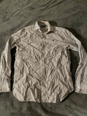 Randig skjorta från Polo Ralph Lauren - Snygg vit och grå randig skjorta från Polo Ralph Lauren i relaxed fit. Klassisk krage, långa ärmar och knappar framtill. Tillverkad i bomull och har den ikoniska lilla loggan broderad på bröstet. Perfekt för en clean och stilren look. Står storlek 8 men är stor i storleken. Skriv för fler frågor!👍