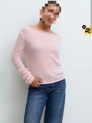 Stickad tröja - Ljusrosa stickad tröja med båtringning och lång ärm. Tröjan har en mjuk, fluffig struktur sopass att den sopass att den känns extra cozy. Passformen är avslappnad och materialet ser ut att vara en blandning av syntet och ull. 