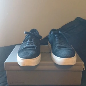 Svarta mockasneakers från Vagabond - Snygga svarta sneakers från Vagabond i mocka med klassisk rund tå och vita platta sulor. Skorna har snörning och en stilren design som passar till det mesta. Perfekta för dig som gillar en clean och enkel look med lite extra edge. Pris ej hugget i sten!