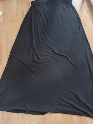 Svart lång långkjol  - En svart långkjol kjom med enkel och rak design. Kjolen är lång och har en mjuk, stretchig känsla i tyget. Perfekt för dig som gillar minimalistisk stil och vill ha något bekvämt och stilrent. Till fötterna på mig (160)kan förekomma katthår men försökt få bort allt! Rollar en extra gång innan postning 