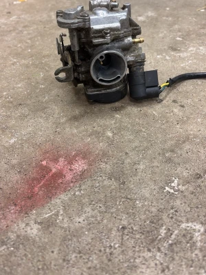 Förgasare till moped eller motorcykel - Metallisk förgasare med elektrisk anslutning, troligen till moped eller motorcykel. Kompakt och robust design i silverfärgad metall med svarta plastdetaljer. Flera anslutningar och justerskruvar synliga. Perfekt för dig som gillar att meka med fordon.