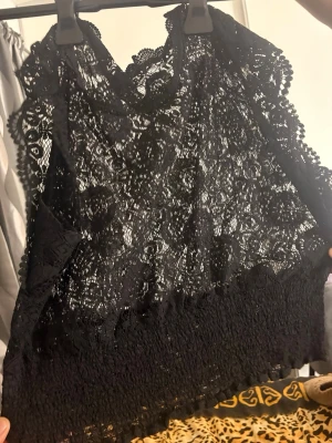 Svart spetsig ärmlös topp från Pieces - Snygg svart ärmlös topp från Pieces med spetsdetaljer och omlottkänsla framtill. Toppen har en croppad passform och är perfekt för att lyfta vilken outfit som helst. Supersnygg att styla med höga jeans eller kjol. Passar i M 