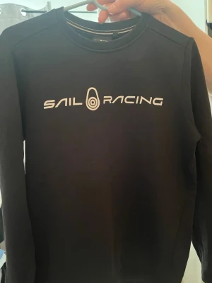Svart Sail Racing hoodie utan luva - säljer denna tröjan för att den inte kommer till användning. Jättefin för dig som gillar stilen och är intresserad.