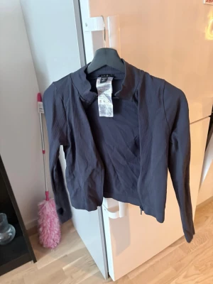 Svart bomberjacka från Divided - Snygg svart bomberjacka från Divided med diskret ribbad struktur. Jackan har dragkedja framtill, ståkrage och långa ärmar. Perfekt för dig som gillar en stilren och enkel look.