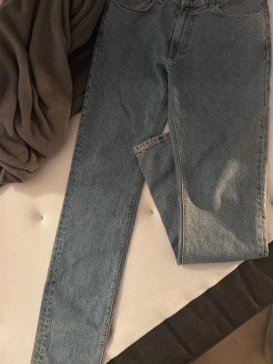 Blå raka jeans i klassisk modell - Säljer ett par blå jeans i klassisk rak modell med hög midja. Jeansen har fem fickor och är tillverkade i ett slitstarkt denimtyg. Perfekta för en avslappnad och tidlös stil.