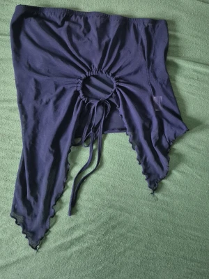 Mörkblå croppad topp med snörning - Trendig mörkblå croppad topp med snörning och öppen cirkeldetalj framtill. Toppen har asymmetrisk nederkant och vågiga kanter för en edgy look. Perfekt för dig som vill sticka ut med din stil.