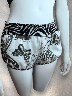 Svarta och vita shorts med zebra och fjärilar - Unika shorts från Brasilien med coolt svartvitt zebramönster. Själva shortsen har ett mixat print med fjärilar, blommor och grafiska detaljer. Materialet känns mjukt och lätt, perfekt för sommarens varma dagar.