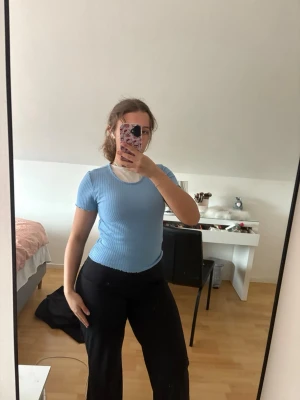 Ljusblå ribbad topp med kort ärm - Säljer en ljusblå ribbad topp med kort ärm och rund halsringning. Toppen är figurnära och har en croppad passform. Perfekt för en trendig och avslappnad stil. (Har ett linne under toppen ifall något ser tokigt ut) säljer en likadan i vitt i flödet vid intresse🥰