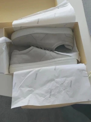 Gråa sneakers från axel arigato - Stilrena gråa sneakers från axel arigato i mocka med vita sulor. Klassisk låg modell med snörning och diskret design som passar till det mesta. Perfekta för dig som gillar minimalistisk stil och vill ha ett par schyssta skor till vardagslooken. passar i alla outfits.