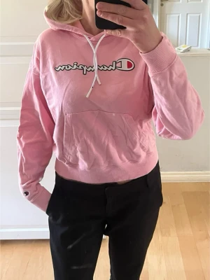 Rosa hoodie från Champion - Snygg rosa hoodie från Champion med vita snören och logga framtill. Hoodien har magficka och ribbade muddar vid ärmslut och midja.  Mycket bra skick