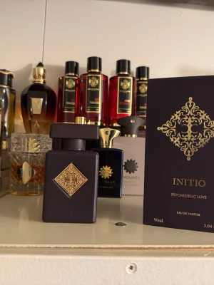 Initio Psychedelic Love Eau de Parfum - Initio Psychedelic Love Eau de Parfum i en lyxig mörklila flaska med guldfärgad dekor och matchande kartong. Flaskan har en fyrkantig form och elegant design, perfekt för dig som gillar exklusiva dofter och snygga parfymflaskor i samlingen.