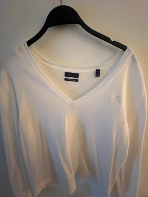 Vit V-ringad tröja från Gant - Vit tröja från Gant i mjuk bomull med V-ringning och diskret broderad logga på bröstet. Klassisk och stilren modell med ribbade muddar vid ärmslut och nederkant. 