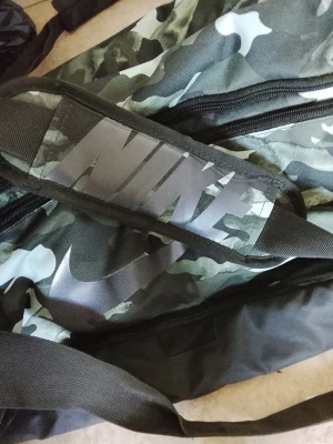 Nike ryggsäck med camomönster HELT NY - Snygg ryggsäck från Nike med grönsvart camomönster och stor logga på framsidan. Tillverkad i slitstarkt tyg med svarta detaljer och dragkedjor. Perfekt för skolan eller gymmet, rymmer allt du behöver och har en cool streetstil. HELY NY. Specifikationer Volym: 60 l Antalet fack: 6 Vikt: 1020 g Längd: 63.5 cm Bredd: 30.5 cm Höjd: 30.5 cm Hjul: Nej Huvudmaterial: 100 % polyester.