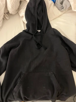 Svart hoodie med magficka - En klassisk svart hoodie med stor huva och dragsko. Hoodien har en rymlig magficka framtill och är tillverkad i mjukt material, perfekt för en avslappnad stil. Passar lika bra till jeans som till mjukisbyxor.
