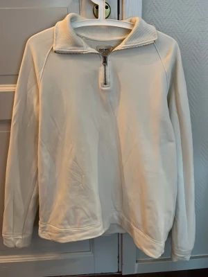 Vit halvzip sweatshirt East West - Säljer en stilren vit sweatshirt från East West med halv dragkedja framtill och hög krage. Tröjan har långa ärmar och är gjord i mjukt material som känns skönt mot huden. Perfekt för dig som gillar en clean och enkel look.