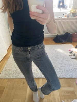 Grå raka jeans - Säljer ett par grå raka jeans med klassisk femficksmodell och medelhög midja. Jeansen har en snygg tvättad look och är tillverkade i ett robust denimtyg. Perfekta för en avslappnad och trendig stil.
